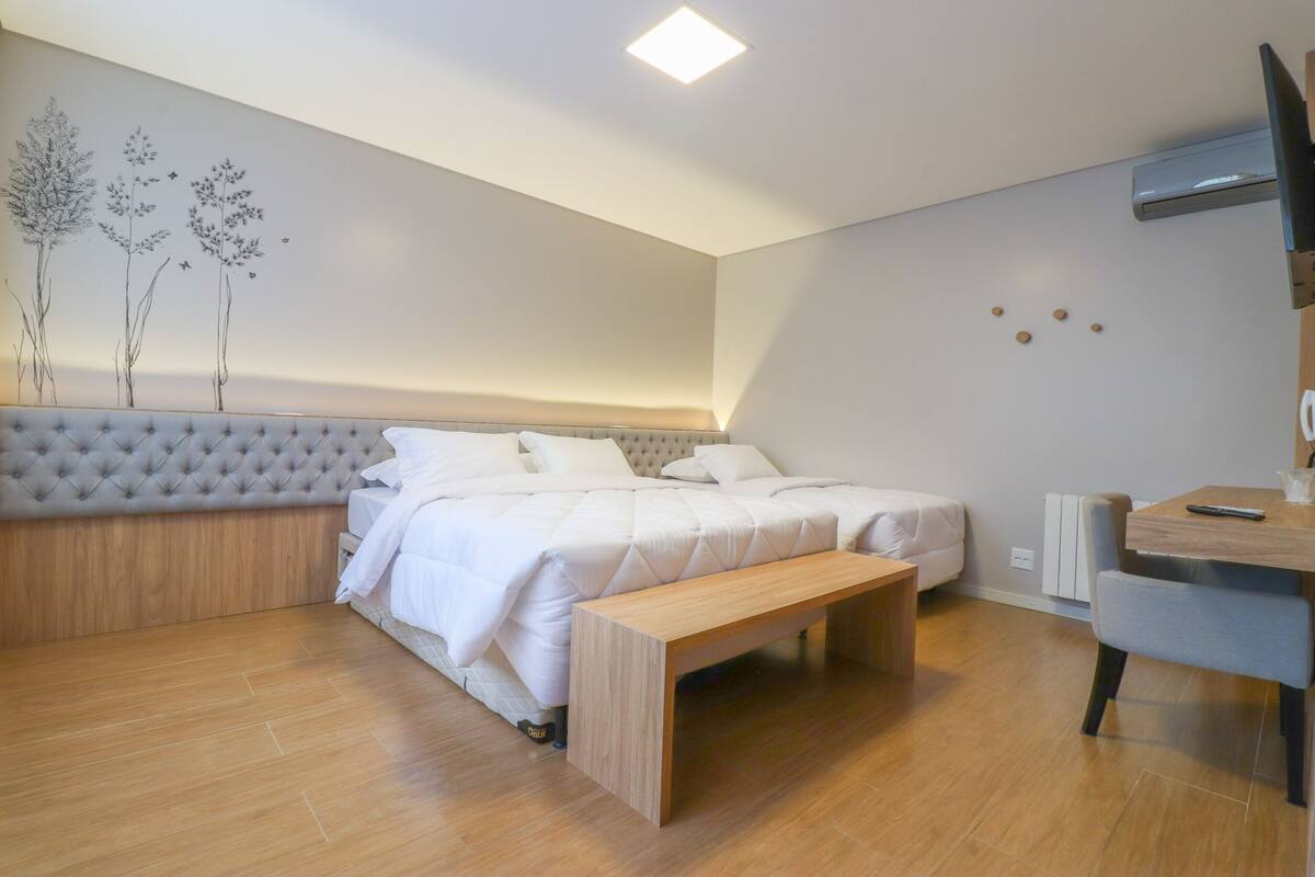 A bedroom with a bed, a bench, a desk, and a wall-mounted TV.