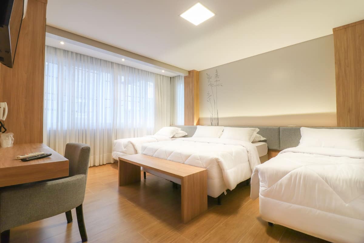 A hotel room with two beds, a desk, and a bench.