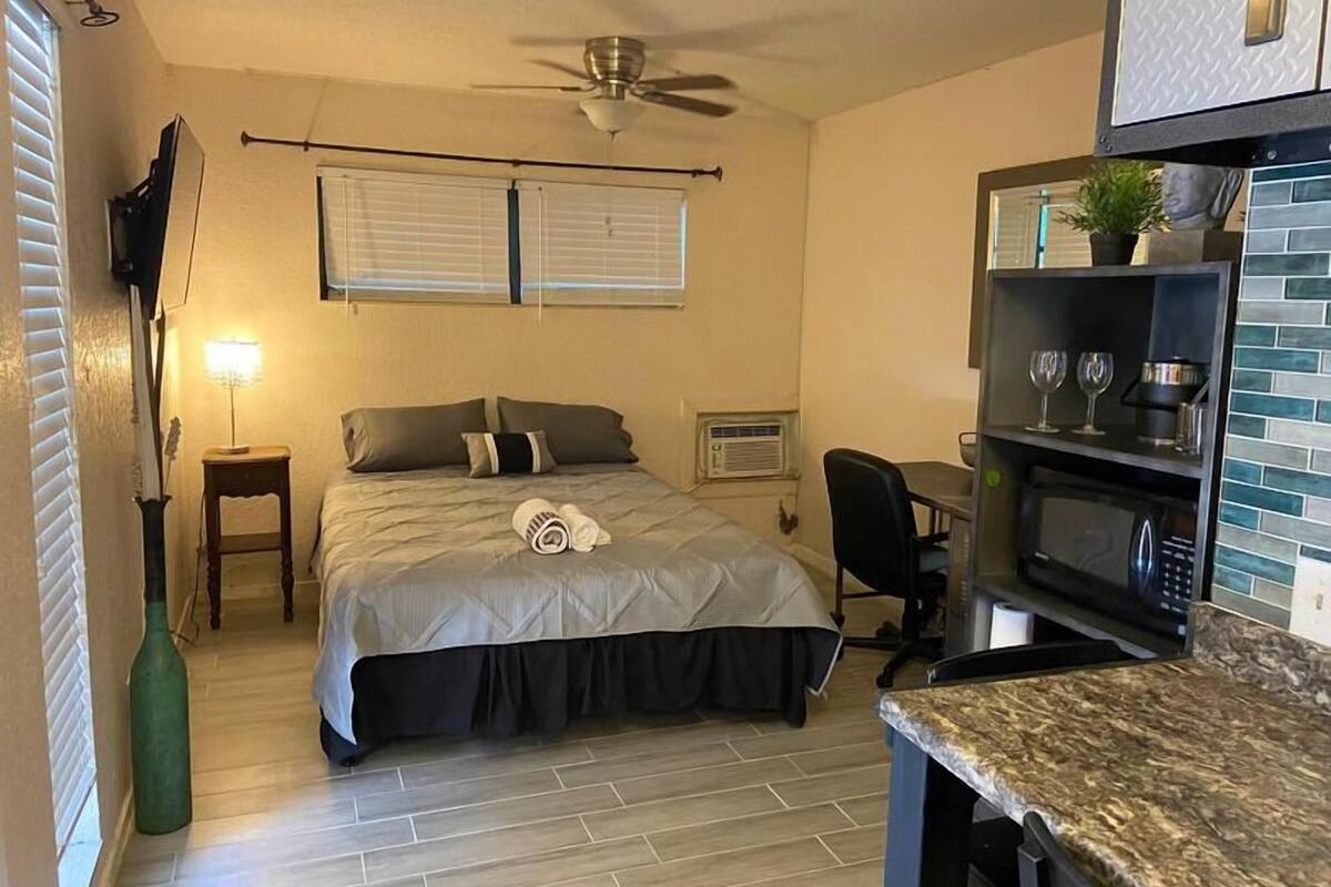 A compact hotel room with a bed, a desk, a microwave, and a ceiling fan.