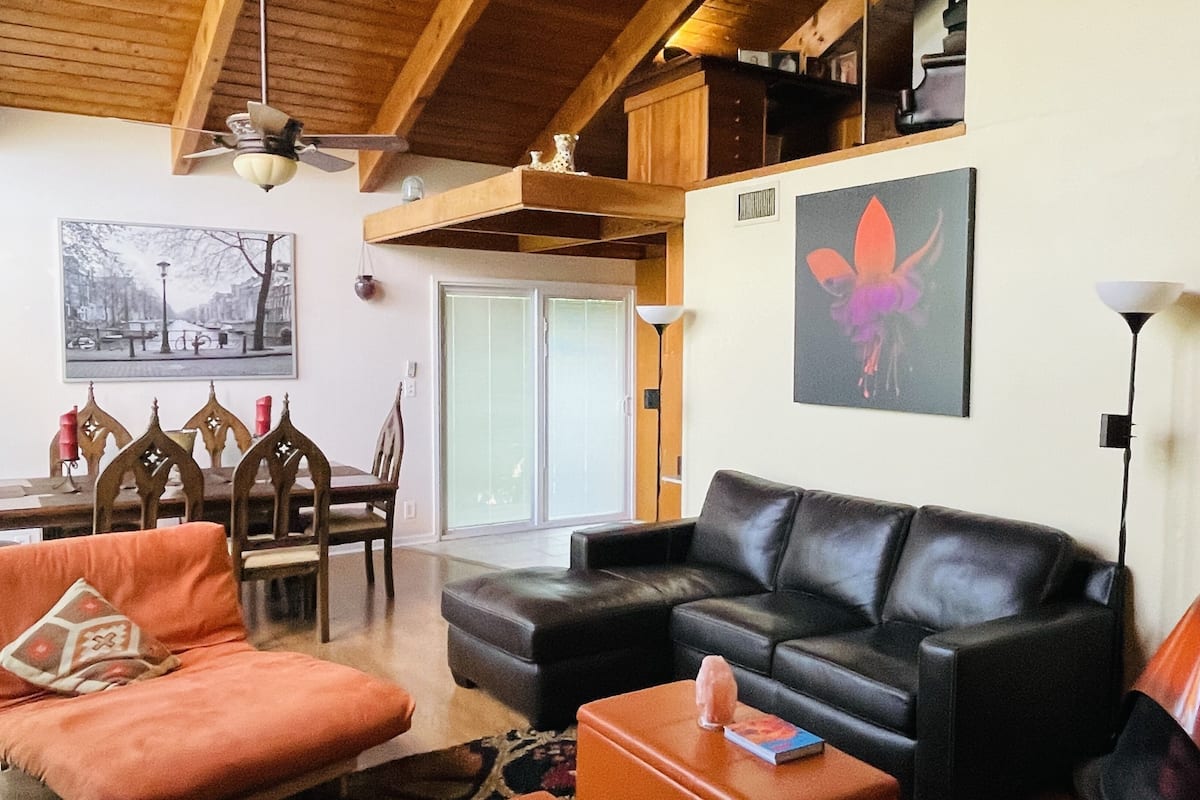 A living room with a black leather sofa, an orange armchair, and a dining area with wooden chairs and a table.
