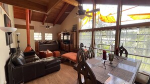 A spacious living area with a wooden ceiling, a sofa, a television, and a dining table with chairs. - Treehouse Apartment Rentals (Pompano Beach)