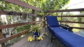 A wooden deck with a blue lounge chair, a potted plant, and a terrarium. - Treehouse Apartment Rentals (Pompano Beach)