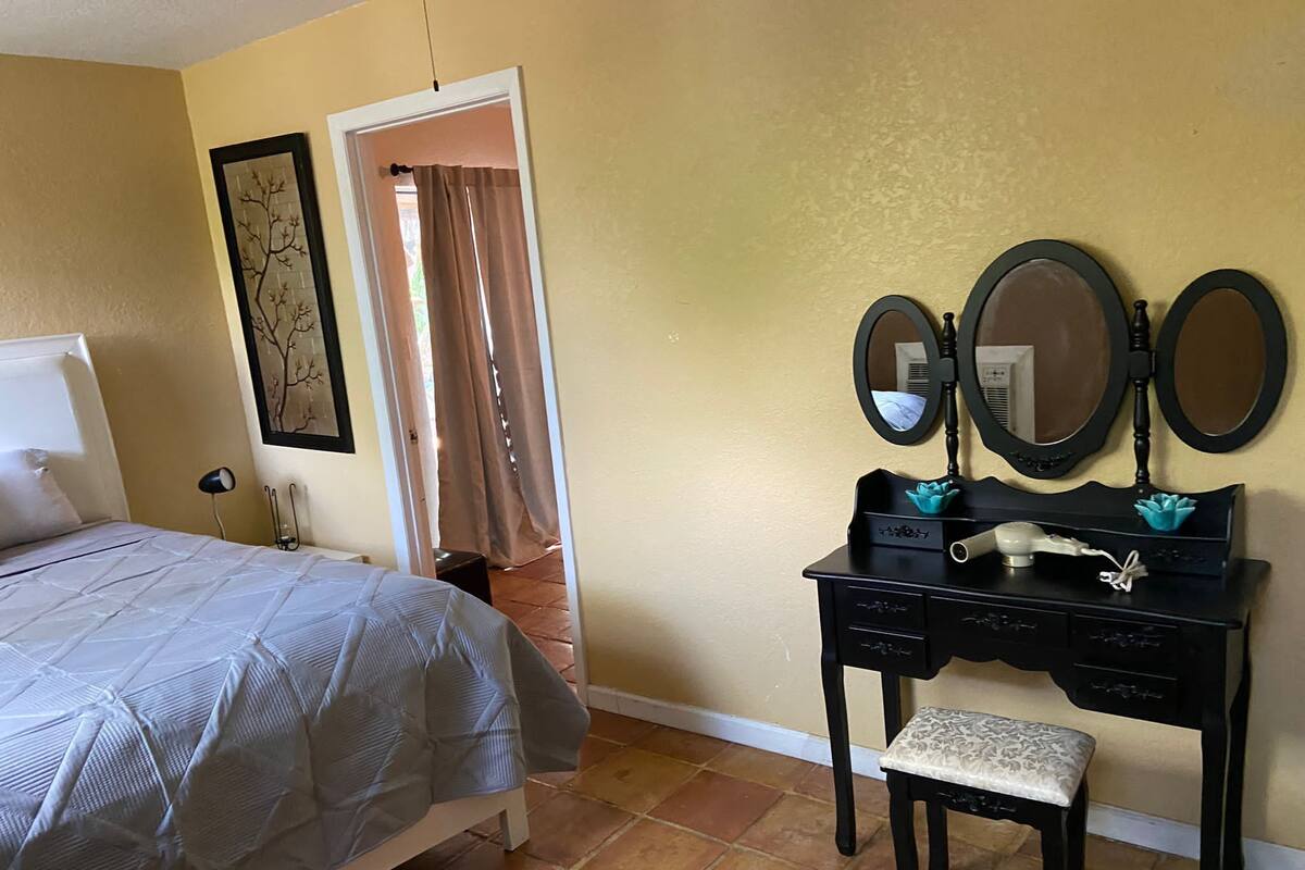 A bedroom with a bed, a dresser with a mirror, and a door leading to another room.