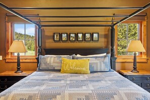 Een hemelbed met een sprei, een kussen met de tekst 'Welkom' en ingekaderde foto's op het hoofdeinde.