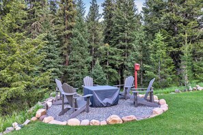 Een rond zitgedeelte buiten met Adirondack-stoelen en een tafel, omgeven door een grindpad en een rotsrand, met een achtergrond van dichte altijdgroene bomen.