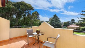 A balcony with two wicker chairs and a small table, surrounded by a beige wall and a tiled floor. - Mediterranean styled house around the corner form East Beach (Port Fairy)