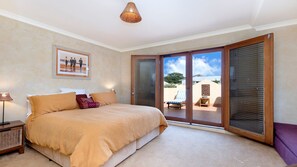 A bedroom with a large bed, a nightstand, a framed picture, and a view of an outdoor area with a chair and a table. - Mediterranean styled house around the corner form East Beach (Port Fairy)