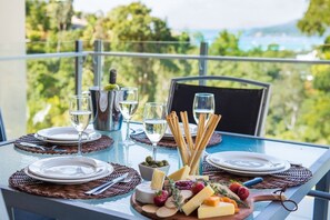 A table set for two with plates, glasses, a bottle, and a cheese board with various cheeses and fruits. - Tulip Oak - Airlie Beach (Airlie Beach)