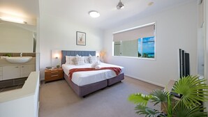 Un dormitorio moderno con una cama grande, mesitas de noche, lavamanos integrado y una ventana con vista al mar.