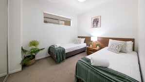 Een hotelkamer met twee bedden, een nachtkastje met een lamp, een potplant en een spiegel aan de muur.