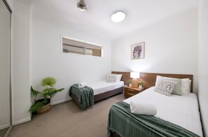 A hotel room with two beds, a bedside table with a lamp, a potted plant, and a wall-mounted mirror. - Tulip Oak - Airlie Beach (Airlie Beach)