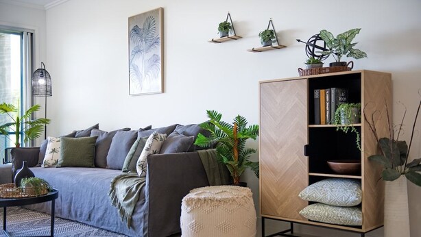 Een woonkamer met een bank, een salontafel, een boekenkast en verschillende planten.
