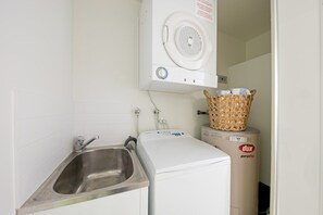 A compact laundry room with a washing machine, a dryer, and a sink. - Tulip Oak - Airlie Beach (Airlie Beach)