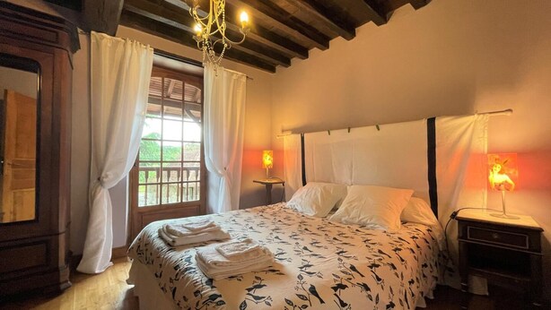A bedroom with a bed, two bedside lamps, a chandelier, and a window with curtains. - Aguerre - Lichos - Gîte (LICHOS)