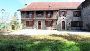 A two-story stone building with a red-tiled roof, a balcony with wooden railings, and a small attached structure with a stone wall and a wooden door. - Aguerre - Lichos - Gîte (LICHOS)