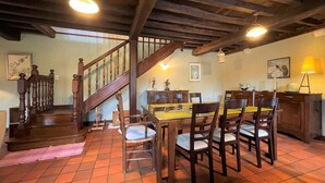 A dining area with a wooden staircase, a dining table with chairs, and a kitchen area. - Aguerre - Lichos - Gîte (LICHOS)