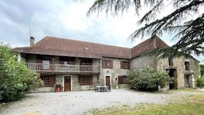 A stone building with a balcony, a gravel courtyard, and a small table with chairs. - Aguerre - Lichos - Gîte (LICHOS)
