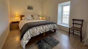 A bedroom with a bed, a chair, a window, and a nightstand with lamps. - Burusenia - Hasparren (HASPARREN)