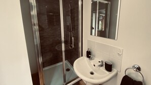 Een moderne badkamer met een douche met glazen wand, een wit wastafelmeubel en een spiegel erboven.