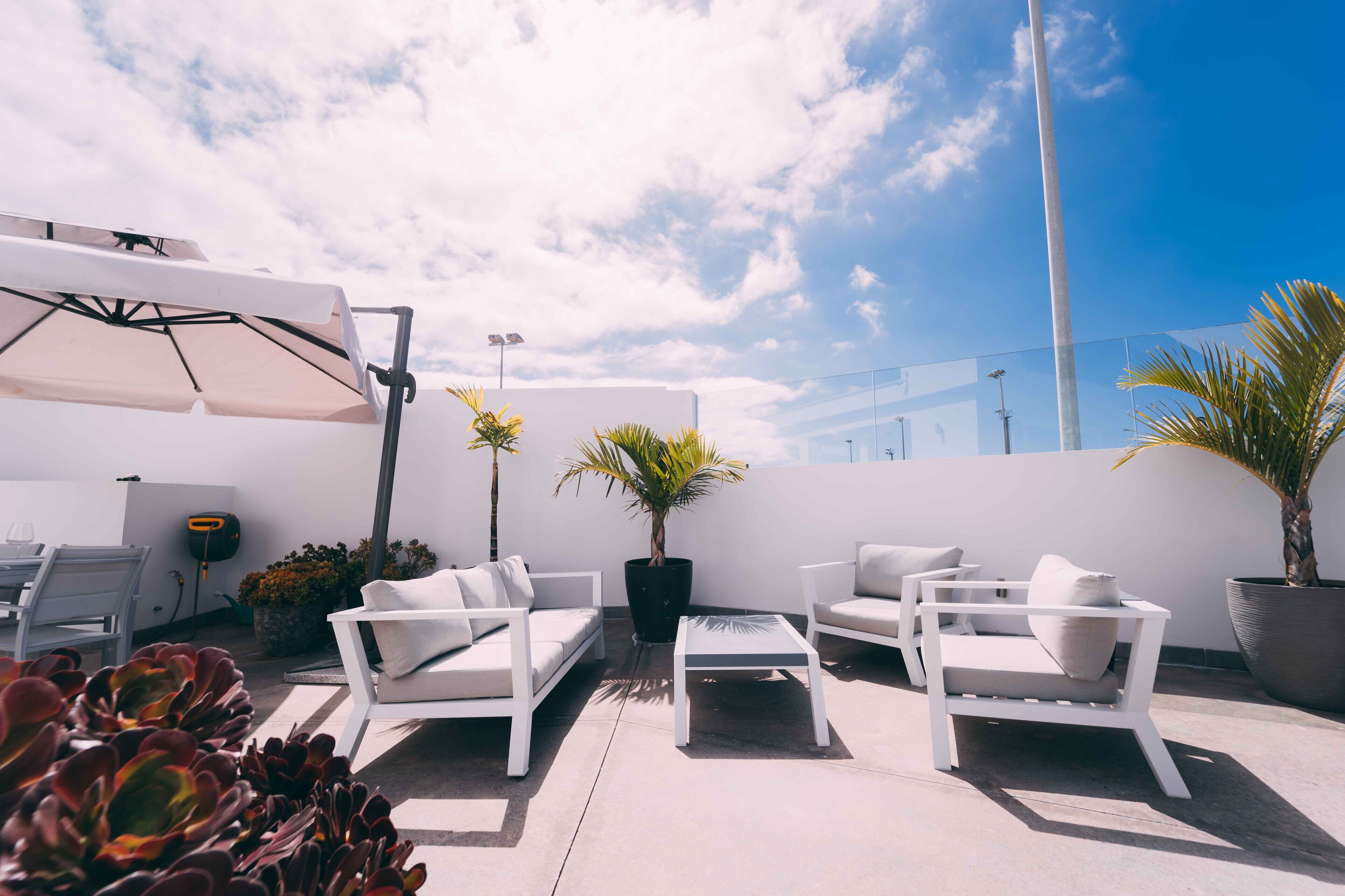 Une terrasse sur le toit, avec des meubles blancs, des plantes en pot et un ciel d’un bleu éclatant.