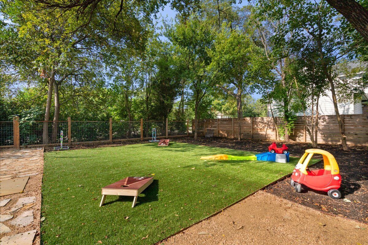 A backyard with a lawn, a wooden play table, and a red toy car.