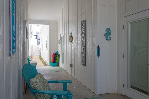 Un corridoio con una sedia e una panca color acquamarina, una porta con la scritta "SEASIDE" e una decorazione a cavalluccio marino.