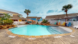 A swimming pool with a 4 FT 6 IN depth marker, surrounded by houses, a fenced area, and lounge chairs. - PB220 Community Pool, Parking for 2 (Port Aransas)