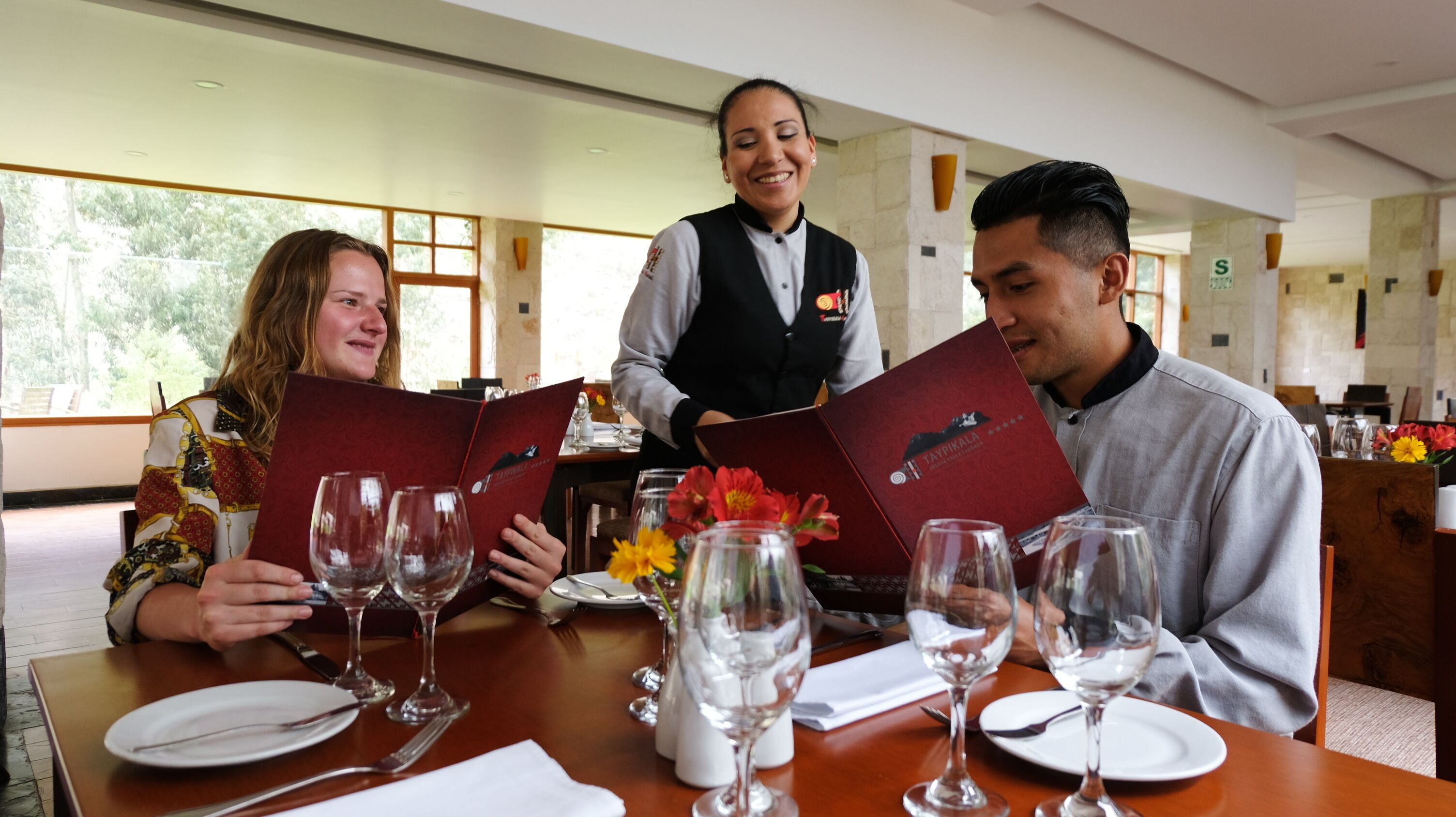 Un restaurante con una mesa lista para tres personas, un menú y copas de vino.