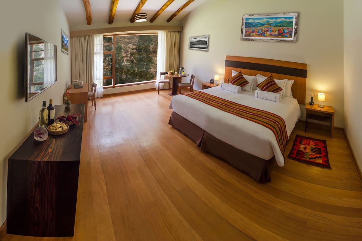 Une chambre spacieuse avec un grand lit, un bureau en bois, une chaise et une vue sur l’extérieur grâce à une grande fenêtre.