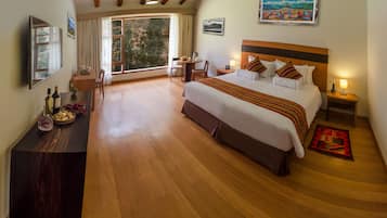 A spacious bedroom with a large bed, a wooden desk, a chair, and a view of the outdoors through a large window.