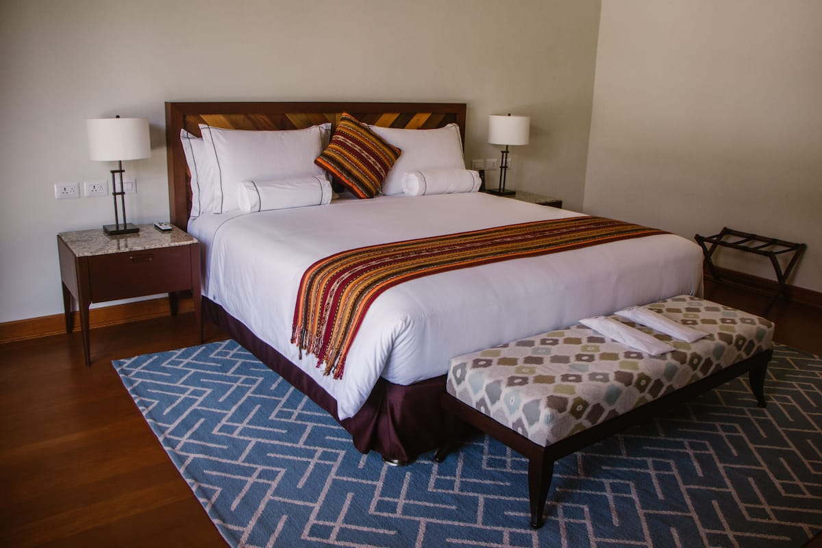 Un lit bien fait, recouvert d’un plaid à motifs, avec un banc assorti et deux lampes de chevet.