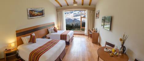 A hotel room with two beds, a dining table, and a view of mountains.