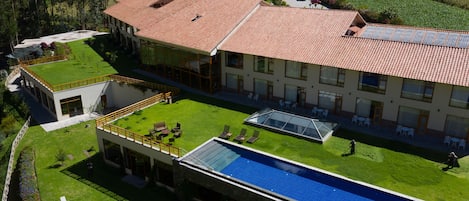 A modern building with a swimming pool, a covered patio, and a well-maintained lawn.