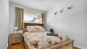 Une chambre à coucher avec un lit en bois, une table de chevet, une lampe et une fenêtre avec des rideaux.
