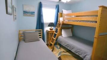 Une chambre avec un lit superposé, un lit simple, un bureau avec une chaise, une fenêtre avec des rideaux et un ventilateur de plafond.