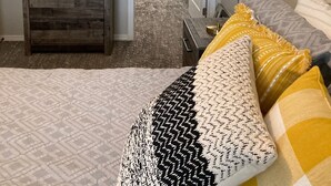 A bedroom with a bed, a dresser, a lamp, and a closet with shelves and hangers. - Downtown at your Doorstep (Anchorage)