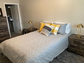 A neatly made bed with patterned bedding, two bedside tables with lamps, and a wooden dresser. - Downtown at your Doorstep (Anchorage)