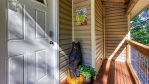 Eine hölzerne Veranda mit einer Bärenstatue, einer Tür mit dekorativen Kassetten und einem farbenfrohen abstrakten Gemälde.