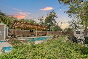 A backyard with a pool, outdoor seating, and a pergola with string lights.