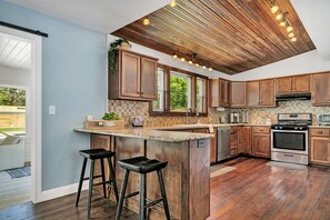 Une cuisine avec des meubles de rangement en bois, un îlot central doté de tabourets, une cuisinière et un four à micro-ondes.