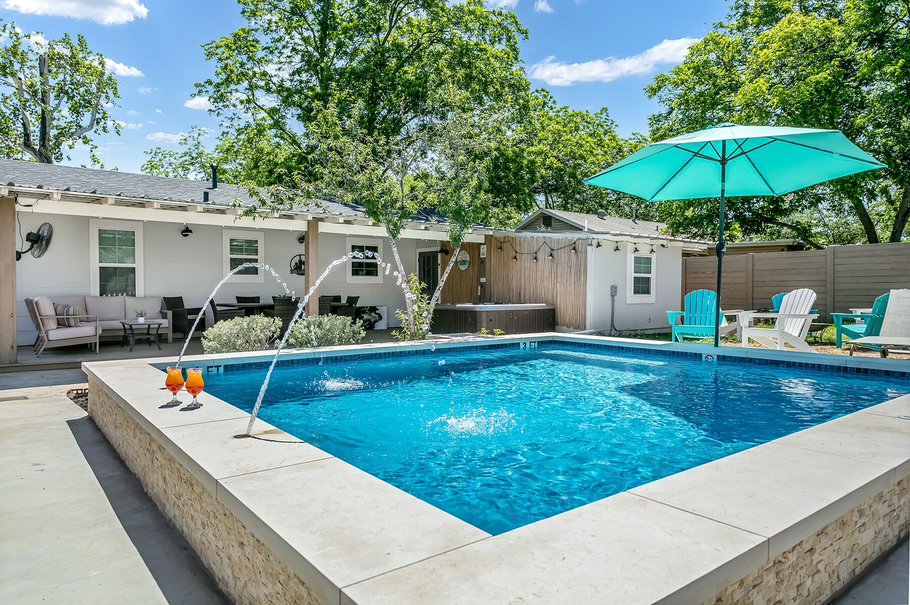 Una piscina rectangular con hidromasaje, rodeada de mobiliario exterior y una valla de madera.