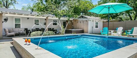 Una piscina rectangular con hidromasaje, rodeada de mobiliario exterior y una valla de madera.
