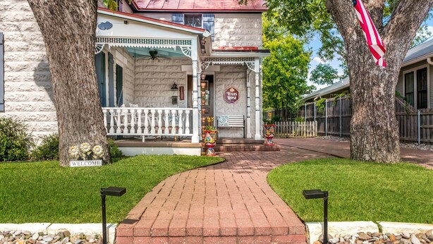 A brick pathway leading to a building with a porch and a sign reading "Texas Rose." - 3/2 Historic Home | Walk to Main | Full Kitchen | WiFi | Hot Tub | Children over 10 welcome! (Fredericksburg)