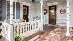 A porch with white railings, a wooden bench, and a door with a sign that reads "Texas Rose." - 3/2 Historic Home | Walk to Main | Full Kitchen | WiFi | Hot Tub | Children over 10 welcome! (Fredericksburg)