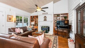 A cozy living room with a fireplace, a television, and a ceiling fan. - 3/2 Historic Home | Walk to Main | Full Kitchen | WiFi | Hot Tub | Children over 10 welcome! (Fredericksburg)