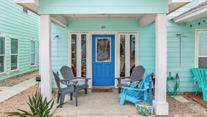Una casa turquesa con puerta azul, dos sillas Adirondack grises y una silla Adirondack azul afuera.