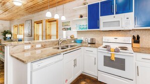 Una cocina con armarios blancos, un microondas azul y un lavamanos de acero inoxidable.