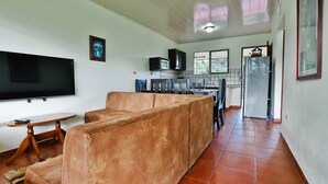 A living room with a sofa, a TV, and a dining area with chairs and a table. - Apartment 10: Condos Vista al Volcan - Second Floor (La Fortuna)