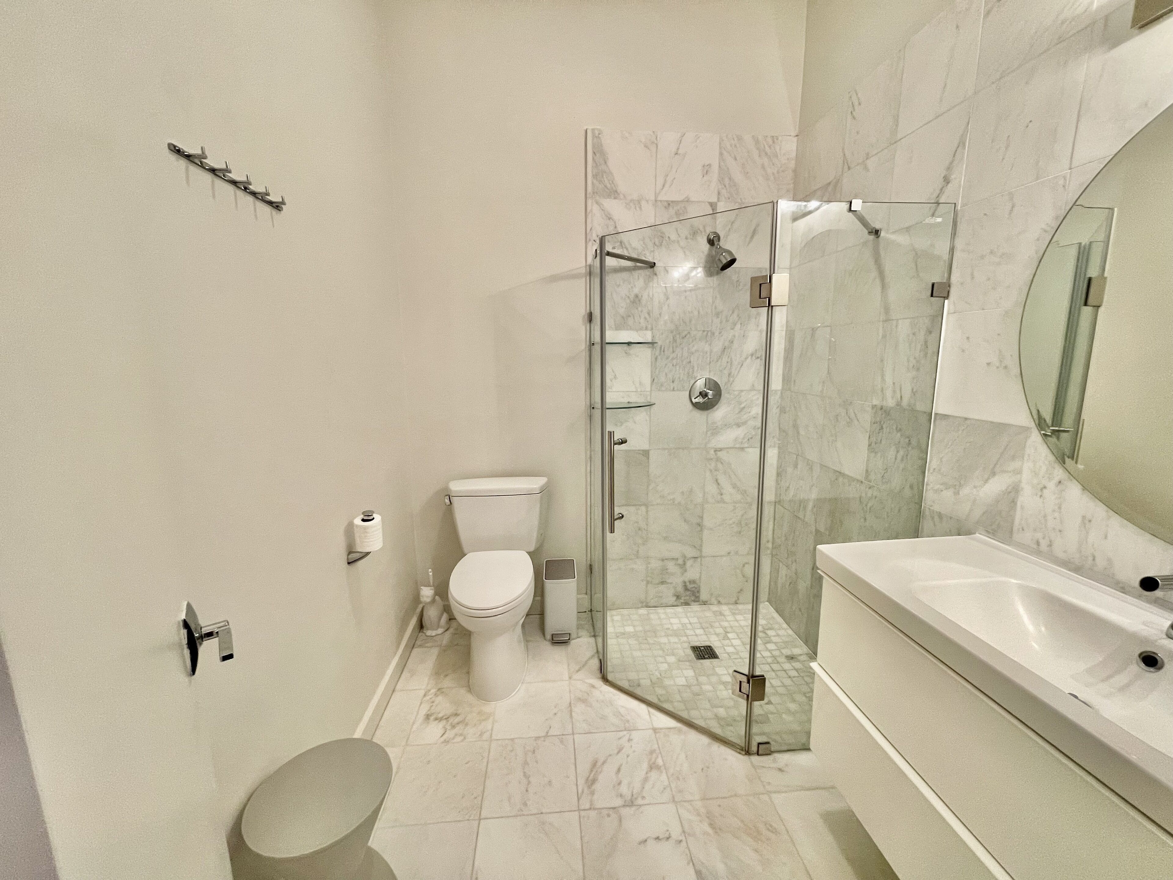 A modern bathroom with a glass-enclosed shower, a toilet, and a large mirror above the sink.