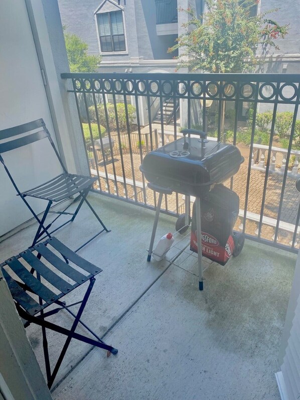 Un balcón con una reja de metal, una silla plegable y una parrilla para barbacoa.